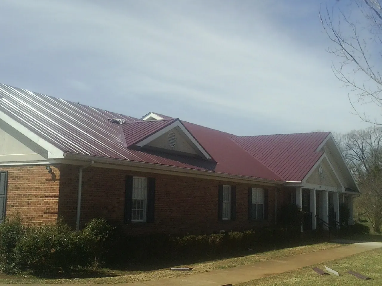 Red metal roof with gabled entries on a long brick building, from a Hail Damage Roof Repair job in Warrendale
