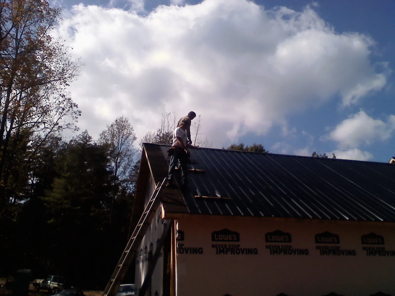 Roofer fastening dark metal panels high against a cloudy sky, from a Roof Inspection job in Warrendale