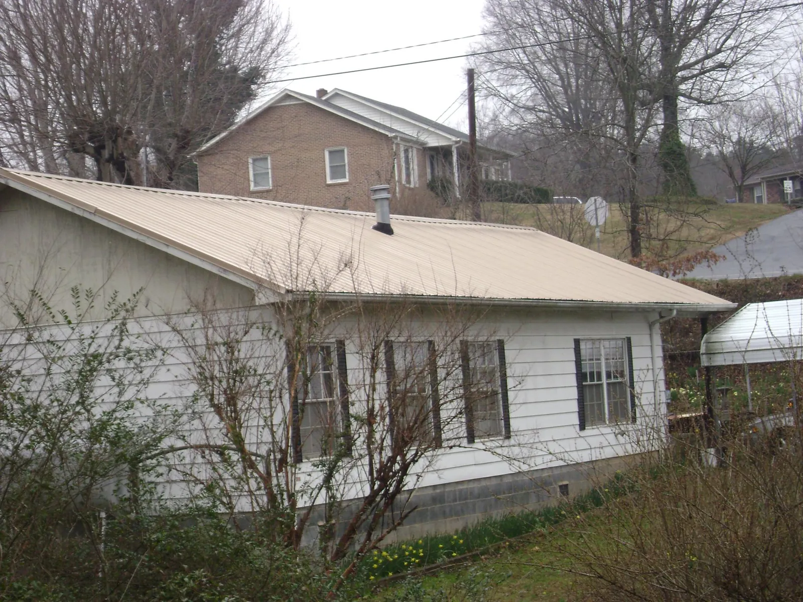 Tan metal roof on a white sided house set into a hillside — Commercial Roofing by Roofing Brothers in Warrendale